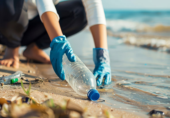 hands picking up plastic bottle from sandy river bank